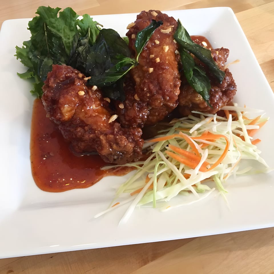 Thai chicken wings with sweet chili sauce, basil, and shredded cabbage and carrots on a white plate.