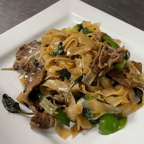 Thai Drunken Noodles with beef, broccoli, and green peppers on a white plate.