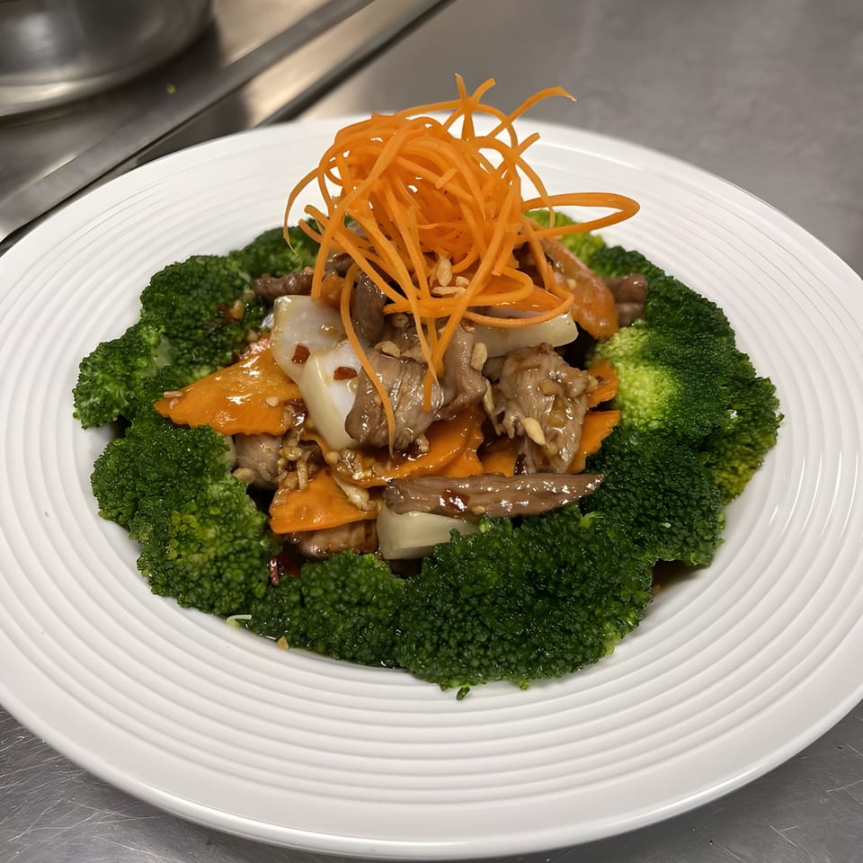 Thai stir-fry with beef, broccoli, carrots, and onions, topped with shredded carrots.