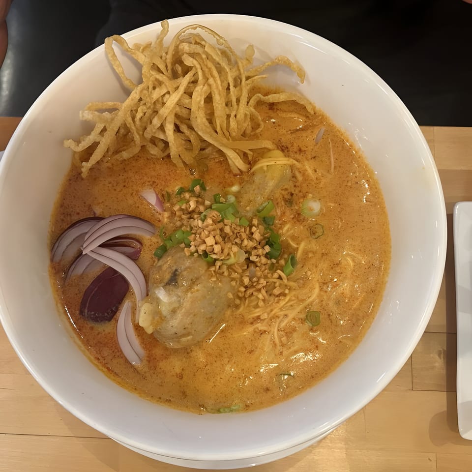 Close-up of a bowl of Khao Soi with chicken, crispy noodles, red onion, and green onions.