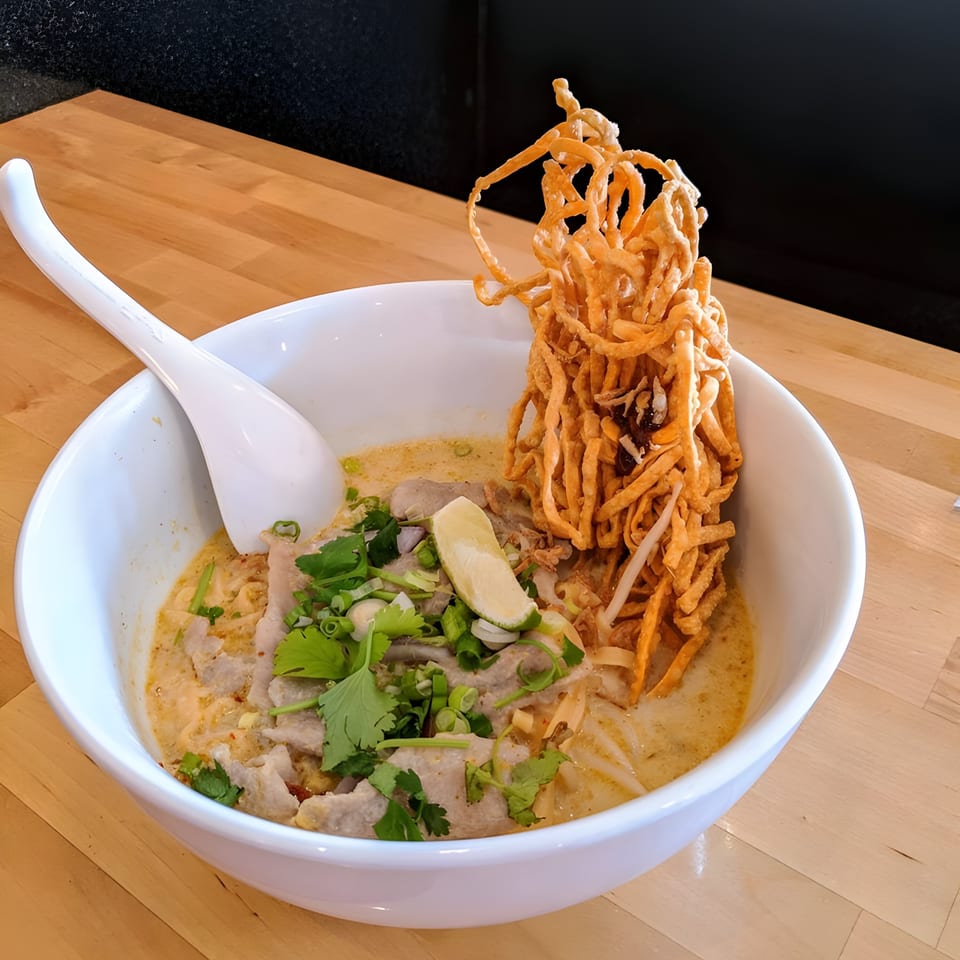 Eat Thai's Khao Soi with crispy noodles, meat, and fresh herbs in a creamy broth.