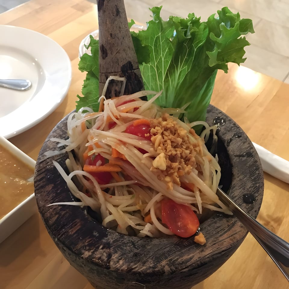 Som Tum, a Thai green papaya salad with tomatoes, peanuts, and lettuce, served in a mortar.