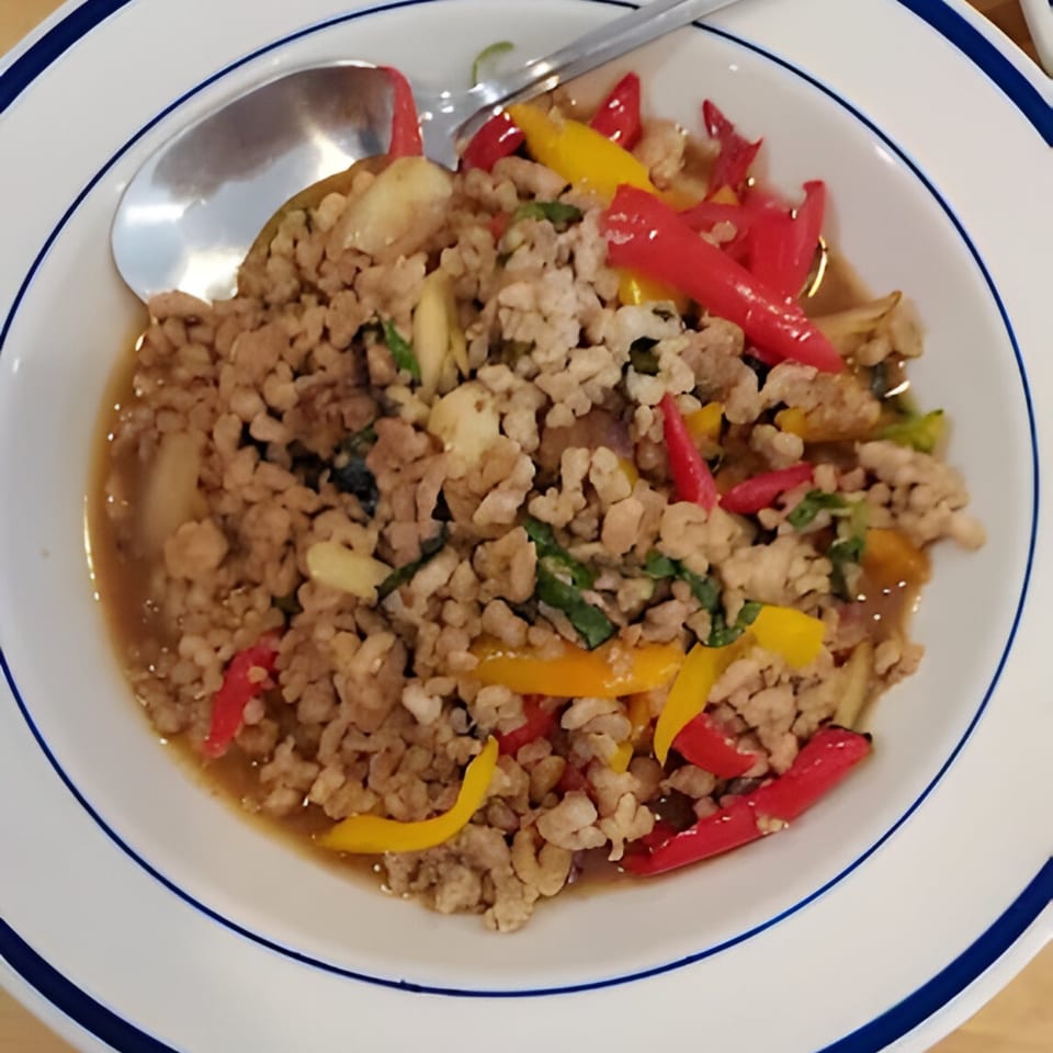 Thai basil chicken with red and yellow bell peppers in a white bowl with a spoon.