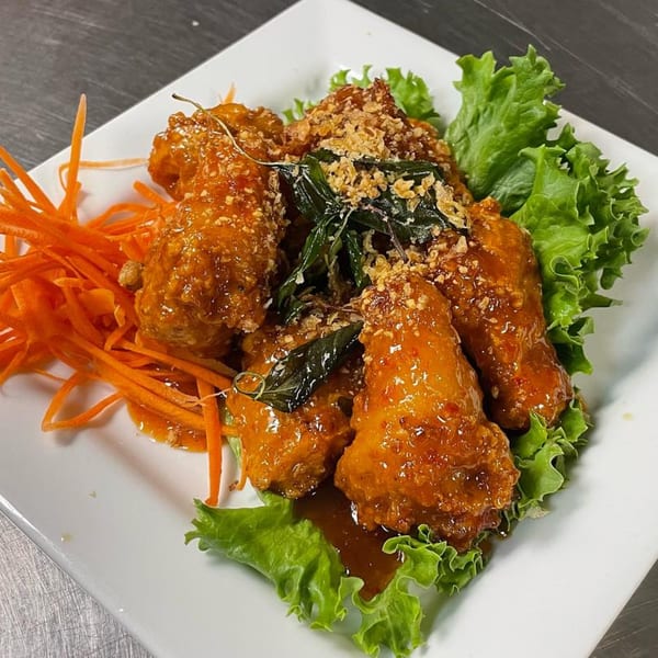 Thai chicken wings with sauce, basil, fried garlic, lettuce, and shredded carrots on a white plate.
