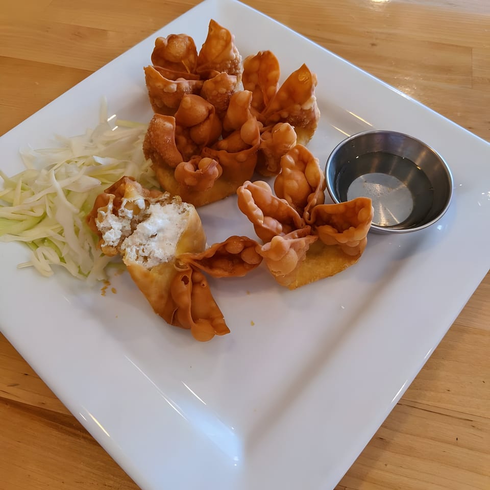 Crispy golden-brown crab rangoons with a creamy filling, shredded cabbage, and dipping sauce on a white plate.